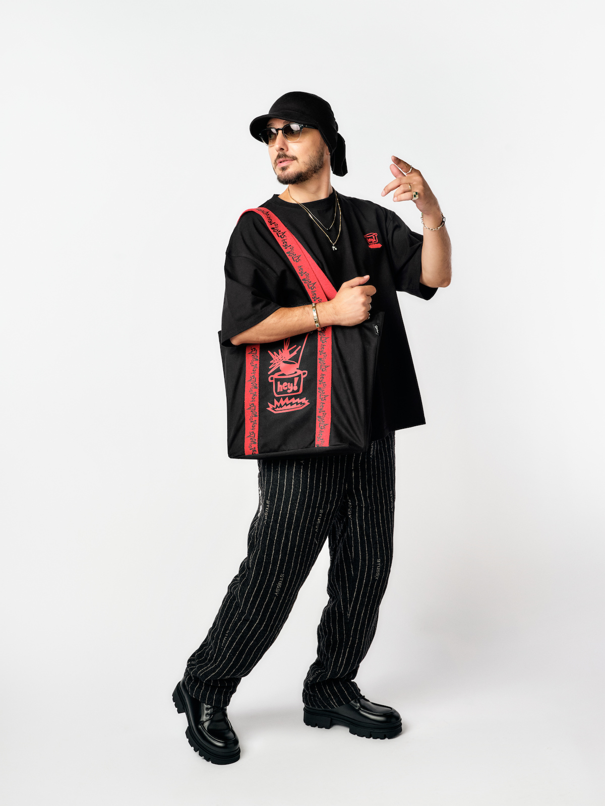 Hey! Douglas, İstanbul Çorbası koleksiyonu fotoğraf çekiminde. Üstünde siyah renkli bir tişört var. Omzunda koleksiyonda kanvas çanta var.